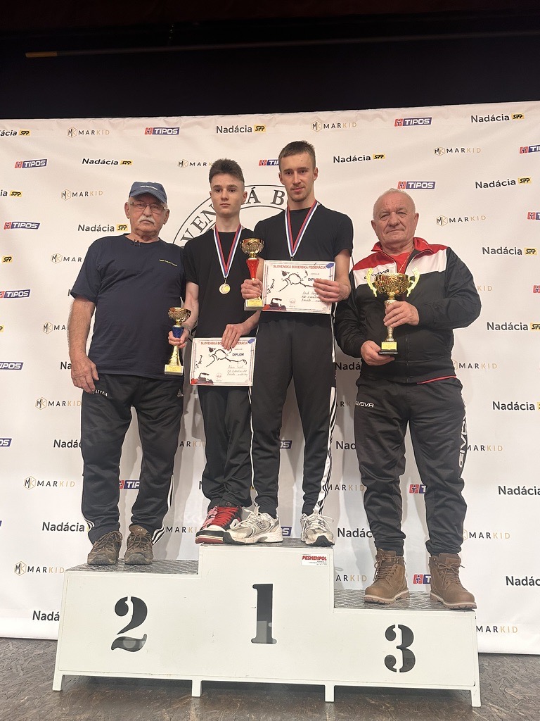 Boxeri na stupňoch víťazov s pohármi a diplomami, vedľa nich tréneri