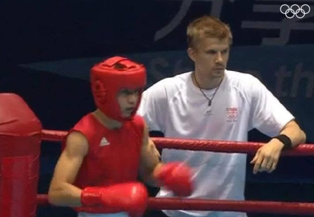 Michal Takács v červenom v rohu ringu, za ním tréner